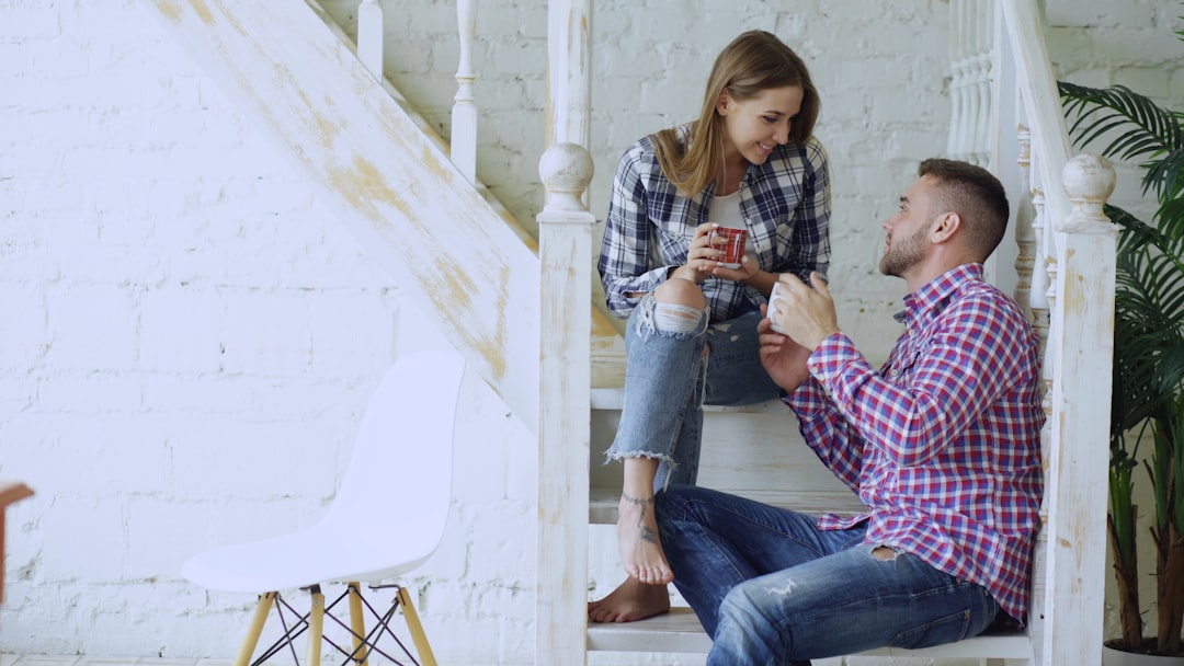 A hopeful couple works together, painting a fresh, clean wall in a bright, sunlit room during a home renovation project.