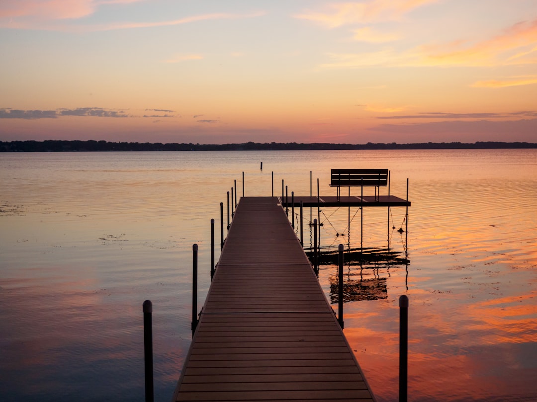A sleek, modern boat lift holding a powerboat out of the clear water next to a dock, highlighting a key piece of waterfront equipment for asset protection.