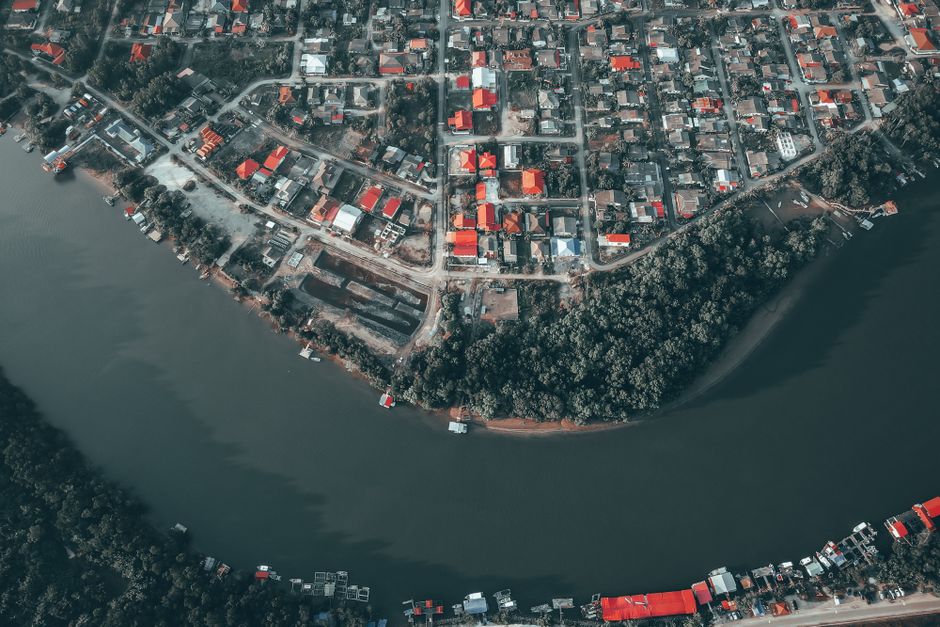 An aerial drone photograph of a stunning, modern luxury house with large glass windows situated directly on the bank of a serene river, representing a high-value property.
