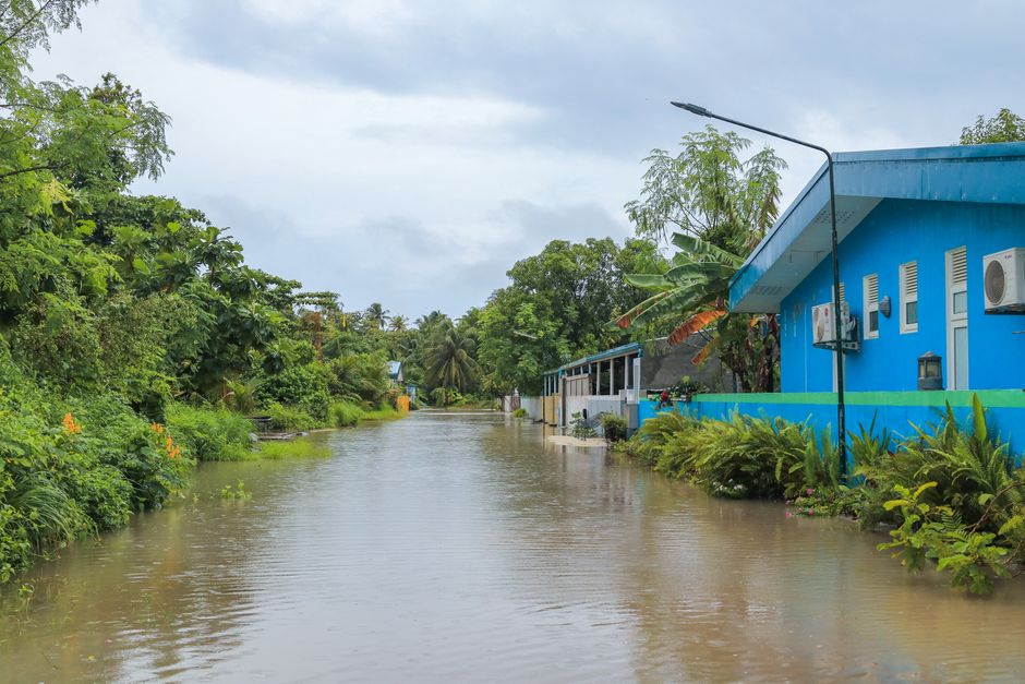Floodwater from a storm covers a residential street, creeping up the lawns towards well-kept suburban homes, illustrating the reality of flood risk.