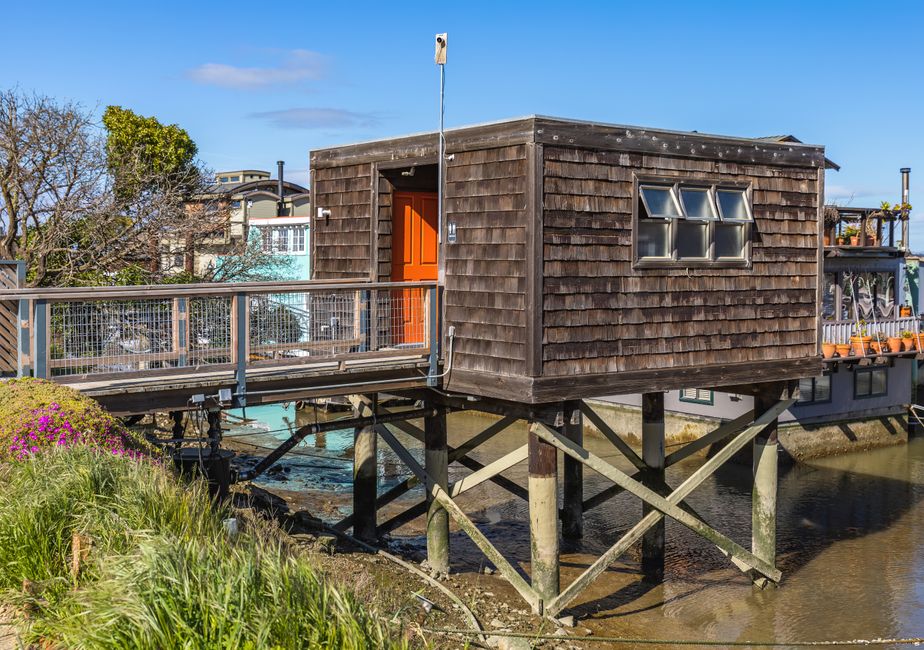 A modern, architecturally designed beach house elevated on tall stilts to protect it from rising tides and storm surges, showcasing smart home fortification.