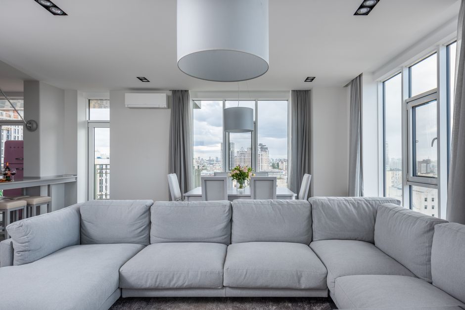 A bright and airy modern living room with large windows offering a stunning view of the water, suggesting a cool and comfortable home fortified against the outdoor heat.